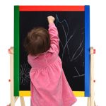 cute little girl writing something with a pink chalk on blackboard