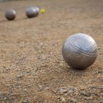 Petanque balls on a sandy pitch with other metal ball in the bac